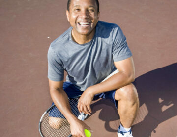 Smiling tennis player kneeling down on court. Vertical